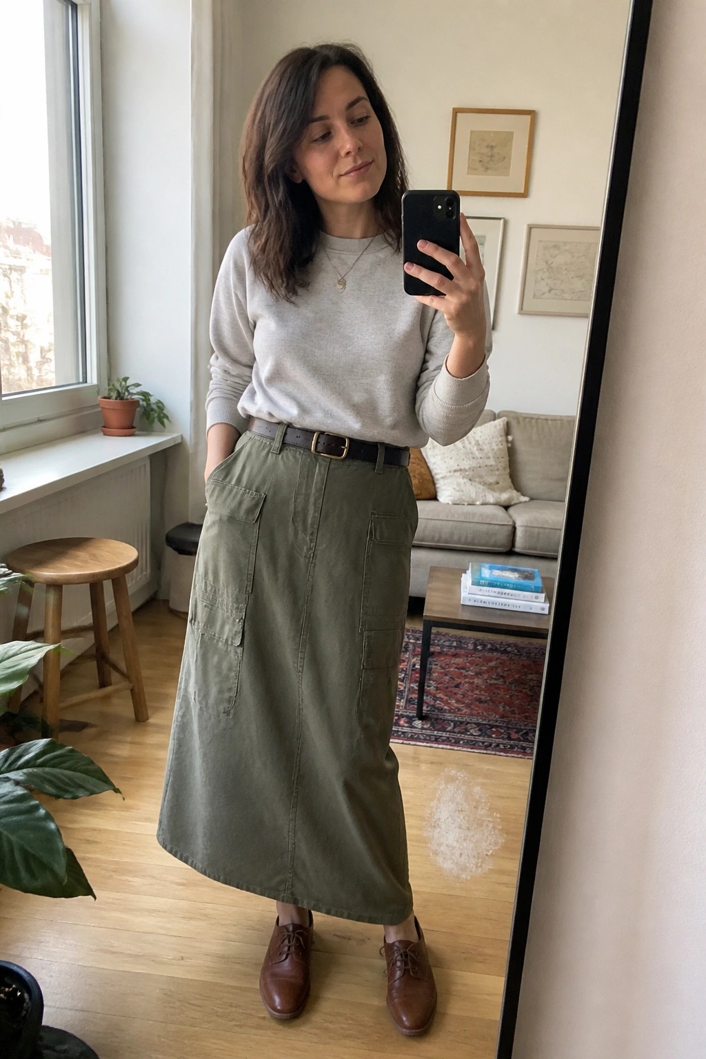 Woman in gray sweater and green cargo skirt taking mirror selfie with phone