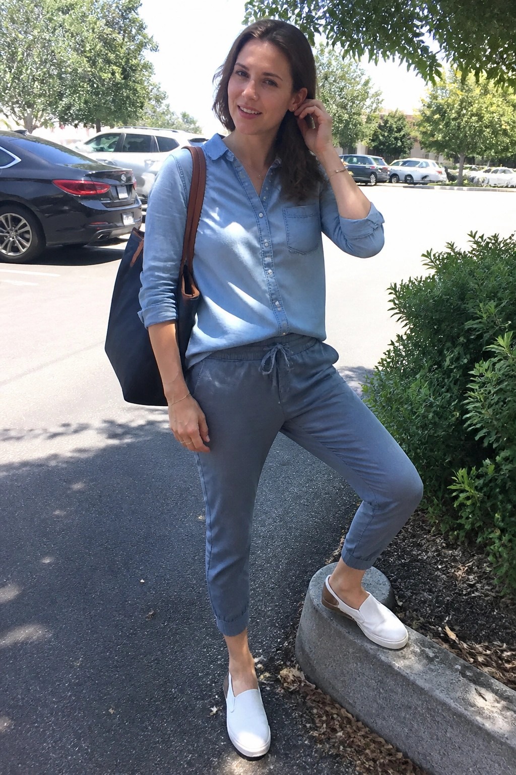 Woman in blue shirt and gray pants posing in sunny parking lot with tote bag