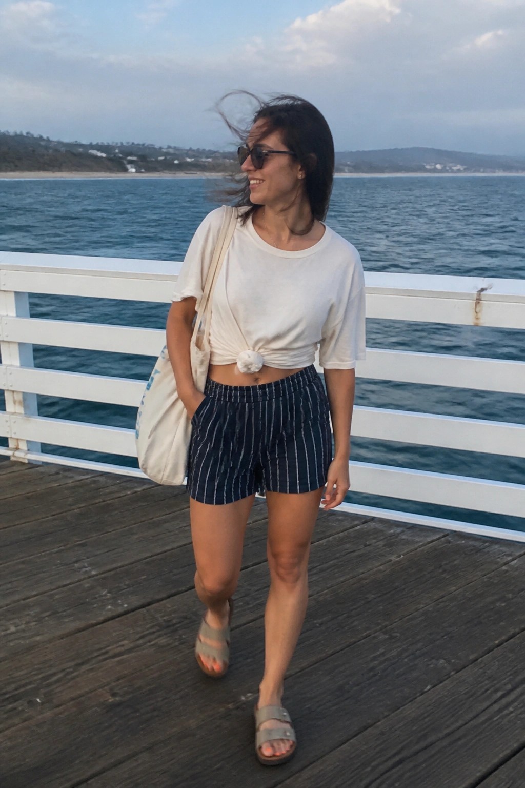 Woman in knotted white tee and striped shorts on windy ocean pier
