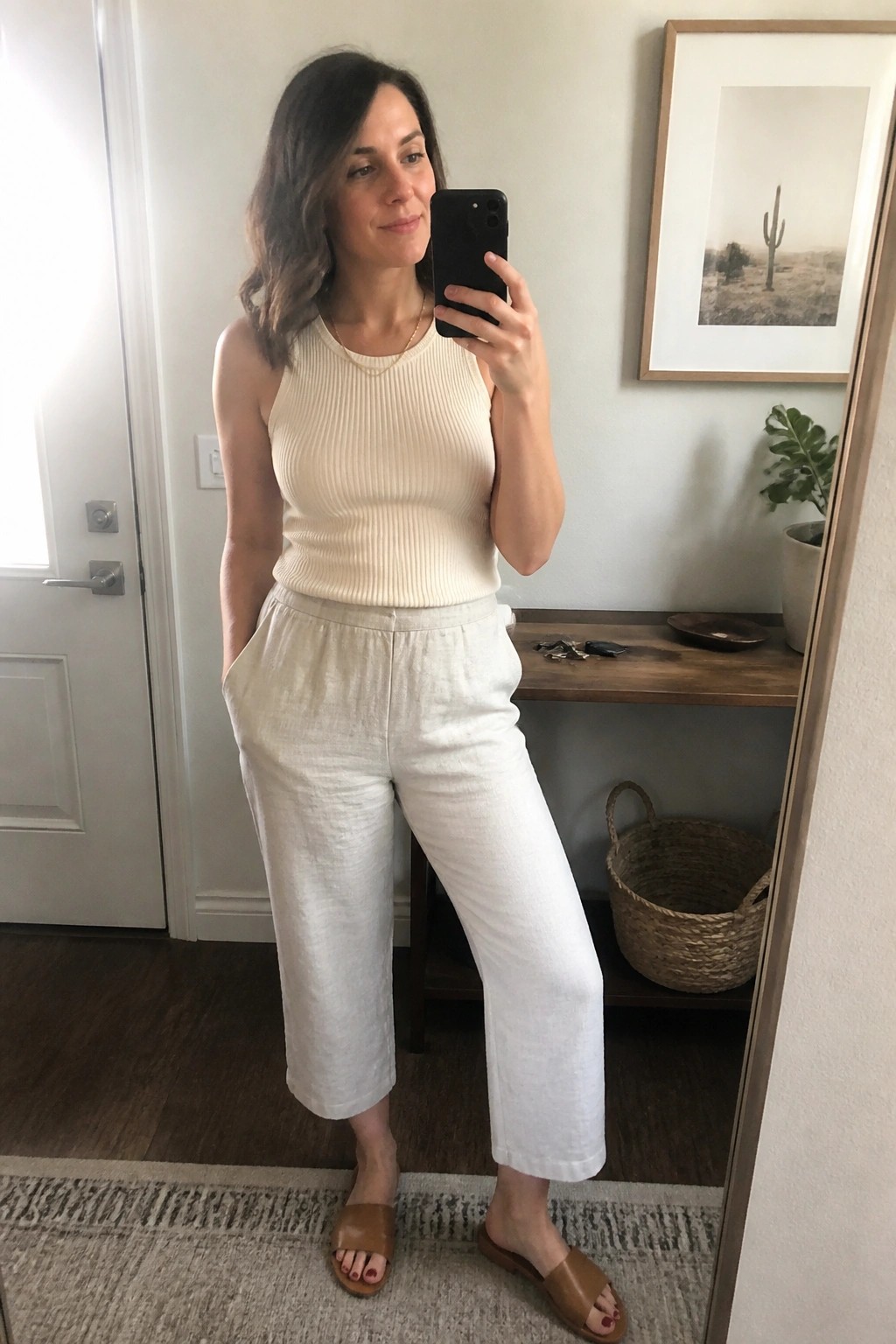 Woman in cream ribbed tank and white linen pants taking mirror selfie