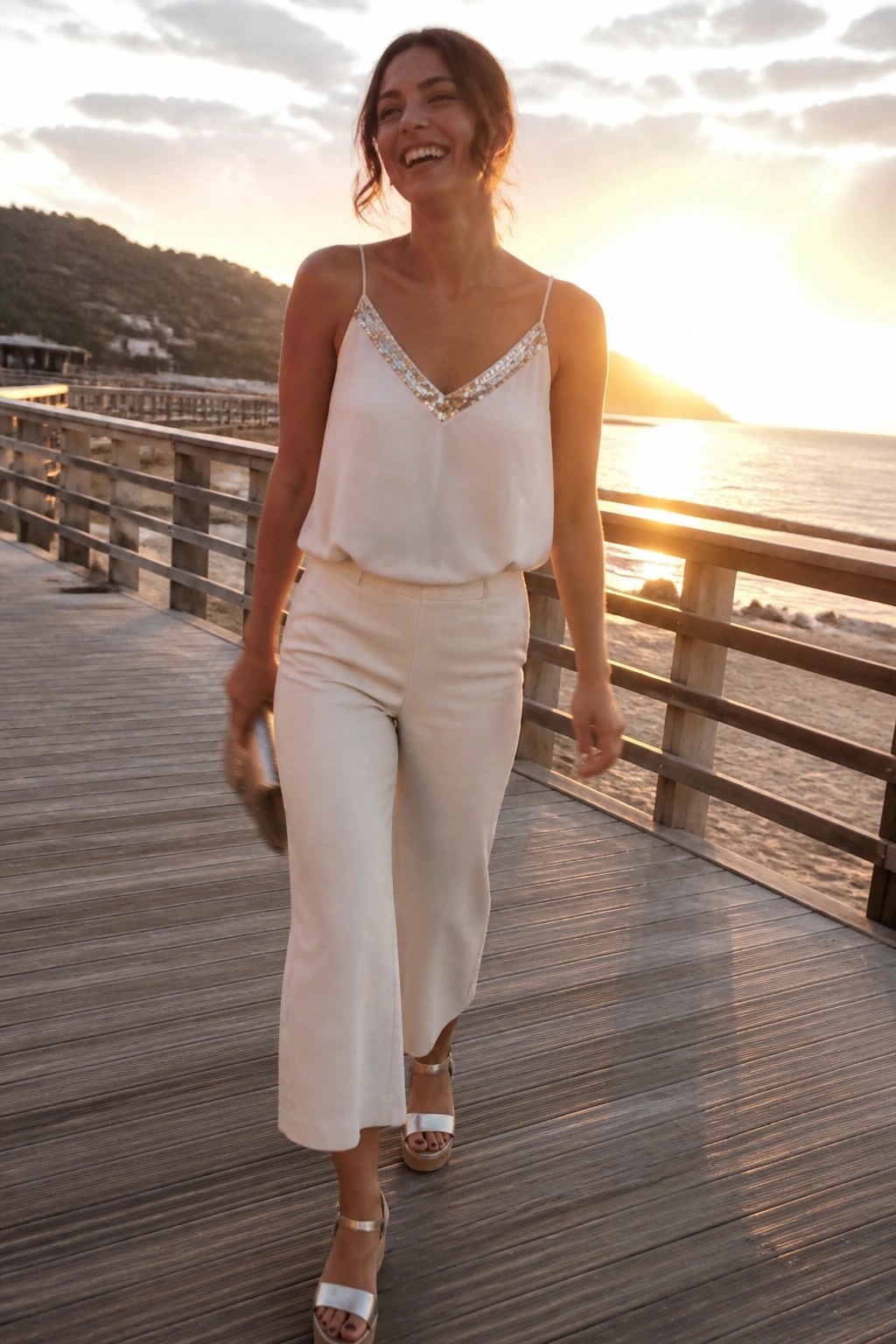 Woman in white sequined top and pants on ocean boardwalk at sunset