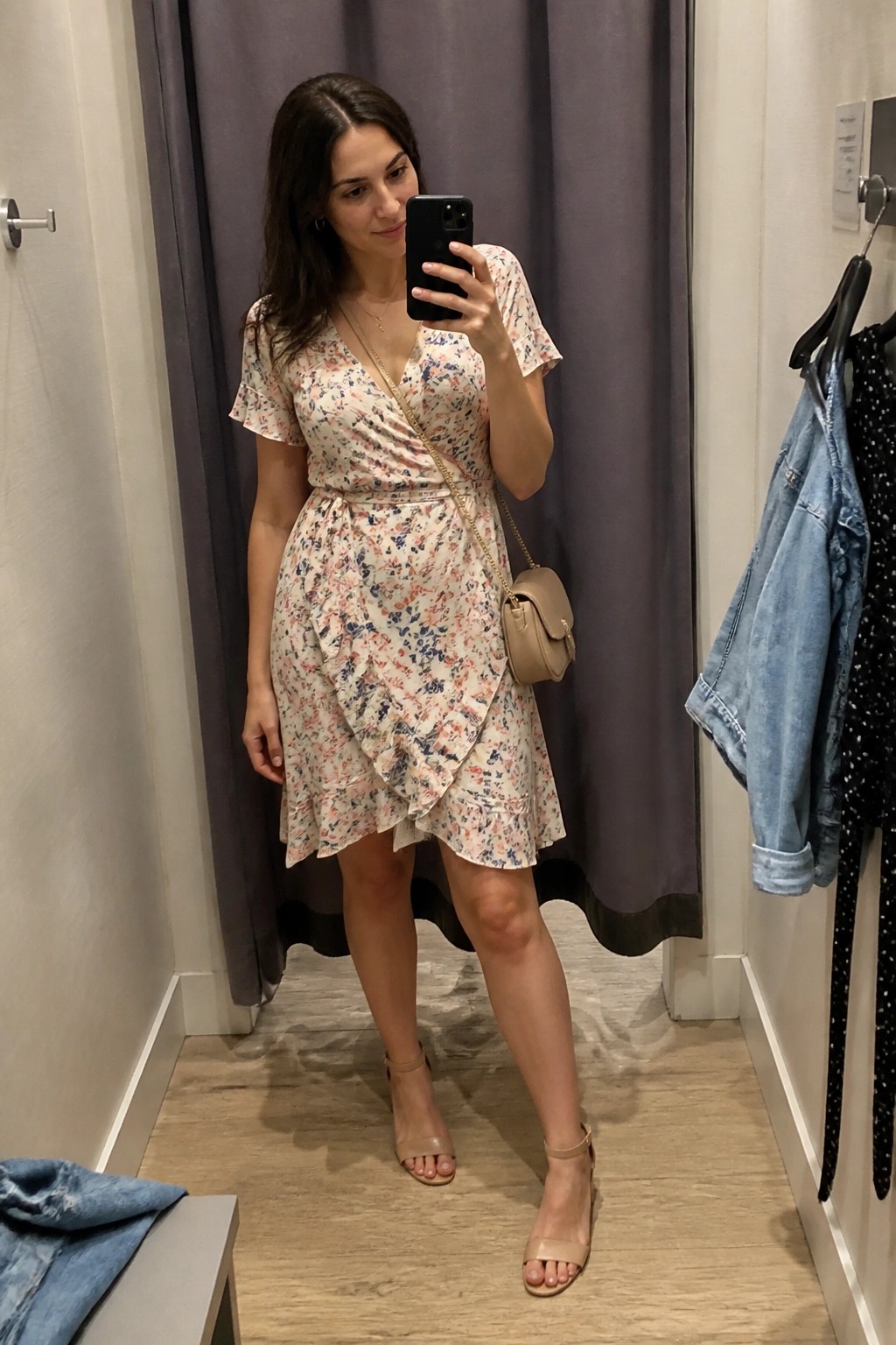 Woman in floral wrap dress taking mirror selfie in fitting room