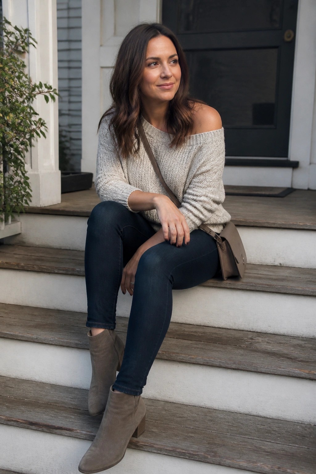 Woman in off-shoulder sweater and jeans sits on wooden porch steps with bag