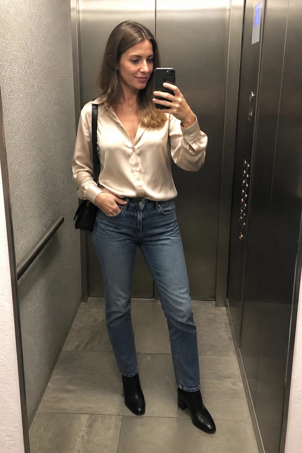 Woman in beige satin blouse and jeans taking elevator mirror selfie