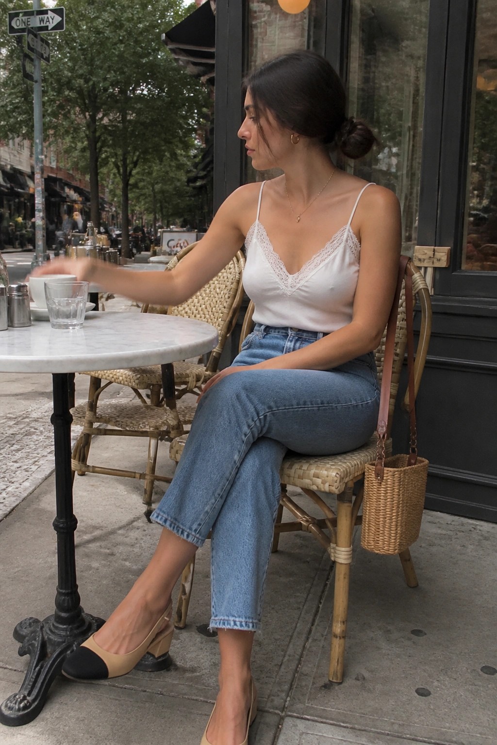 Woman in white lace camisole and jeans at outdoor marble cafe table