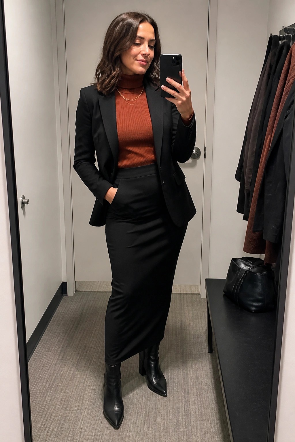 Woman in black blazer and rust turtleneck taking mirror selfie wearing boots