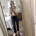 Blonde woman in cream turtleneck and gray puffer vest taking bedroom mirror selfie