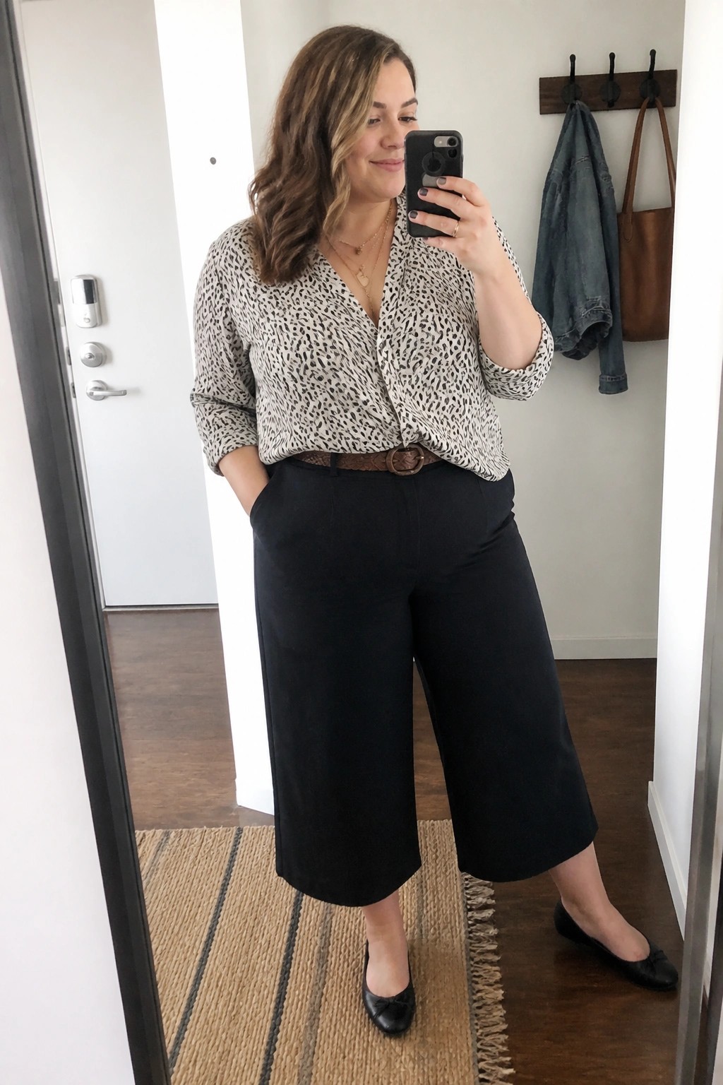 Woman in patterned blouse and black wide-leg pants taking mirror selfie