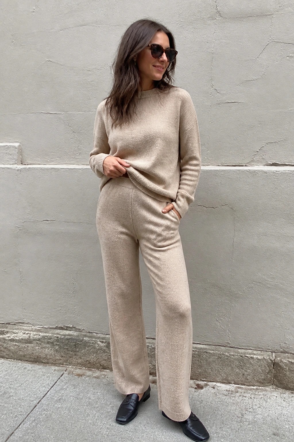 Woman in beige ribbed knit sweater and wide-leg pants with black loafers.