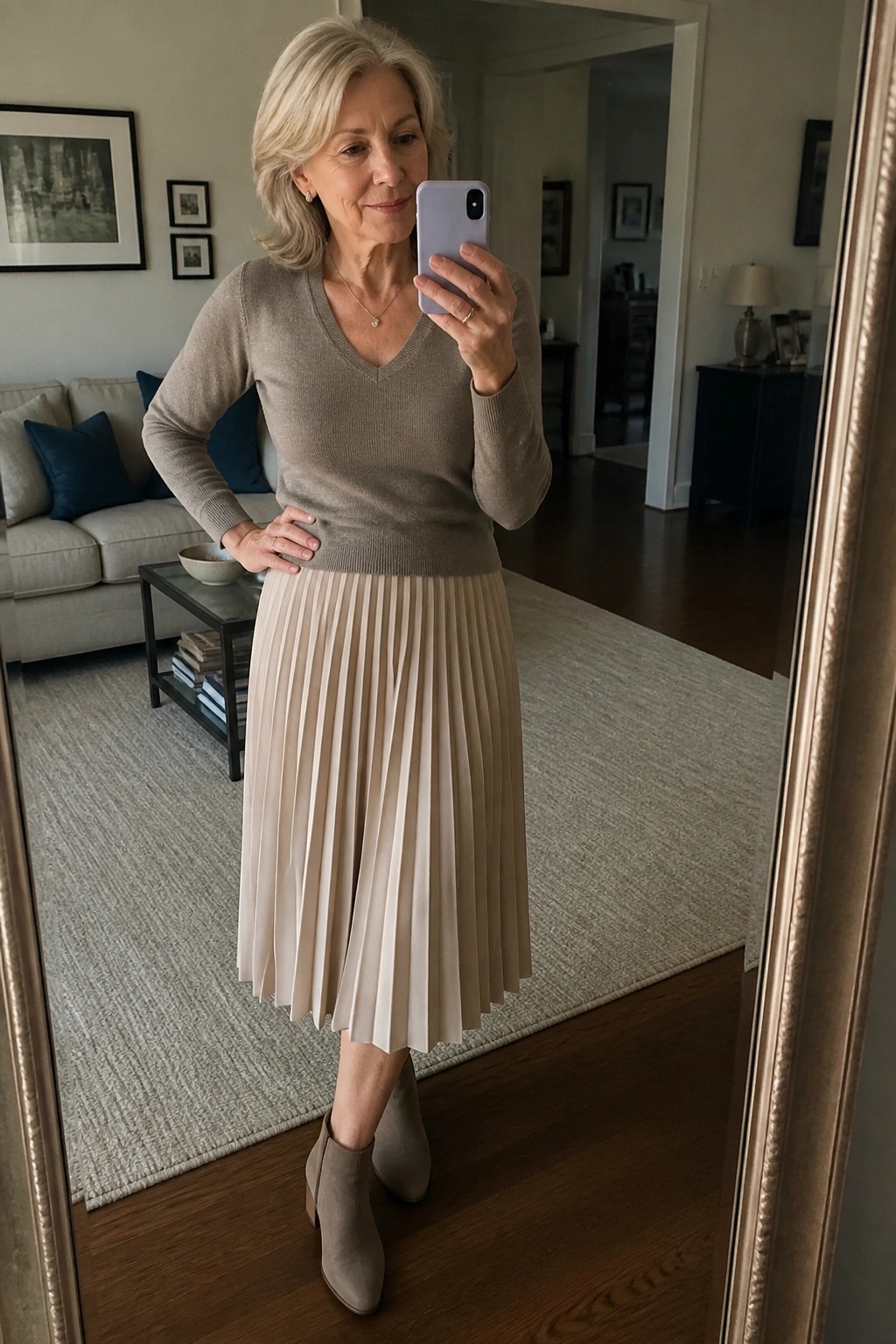 Older woman in beige sweater and pleated skirt taking mirror selfie with phone