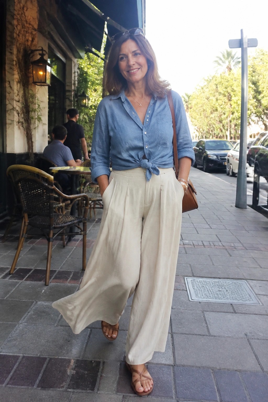 Woman smiling in blue denim shirt knotted at waist with wide beige pants