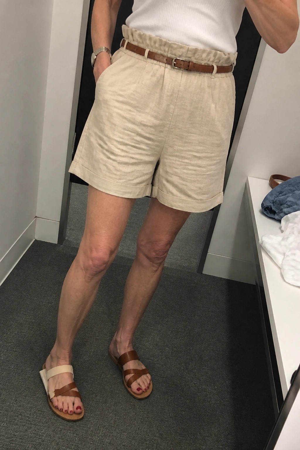 Woman in beige linen shorts with brown belt and sandals in dressing room