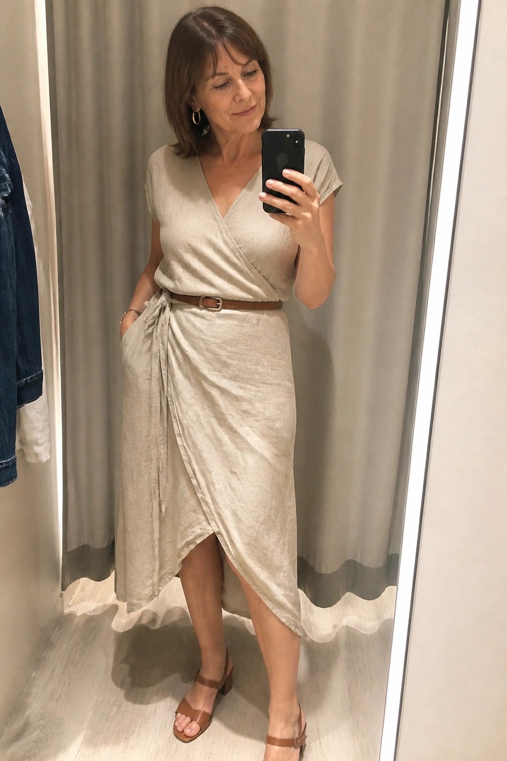 Woman in beige wrap dress taking mirror selfie with brown belt and sandals