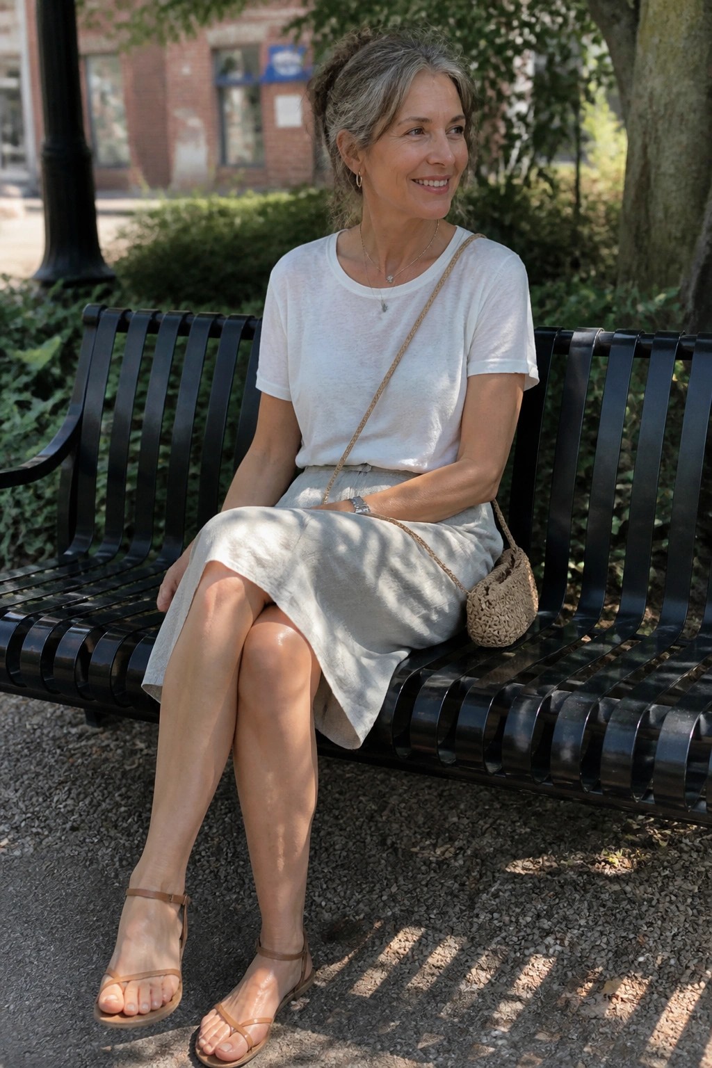Gray-haired woman in white top and beige skirt on black bench with woven bag