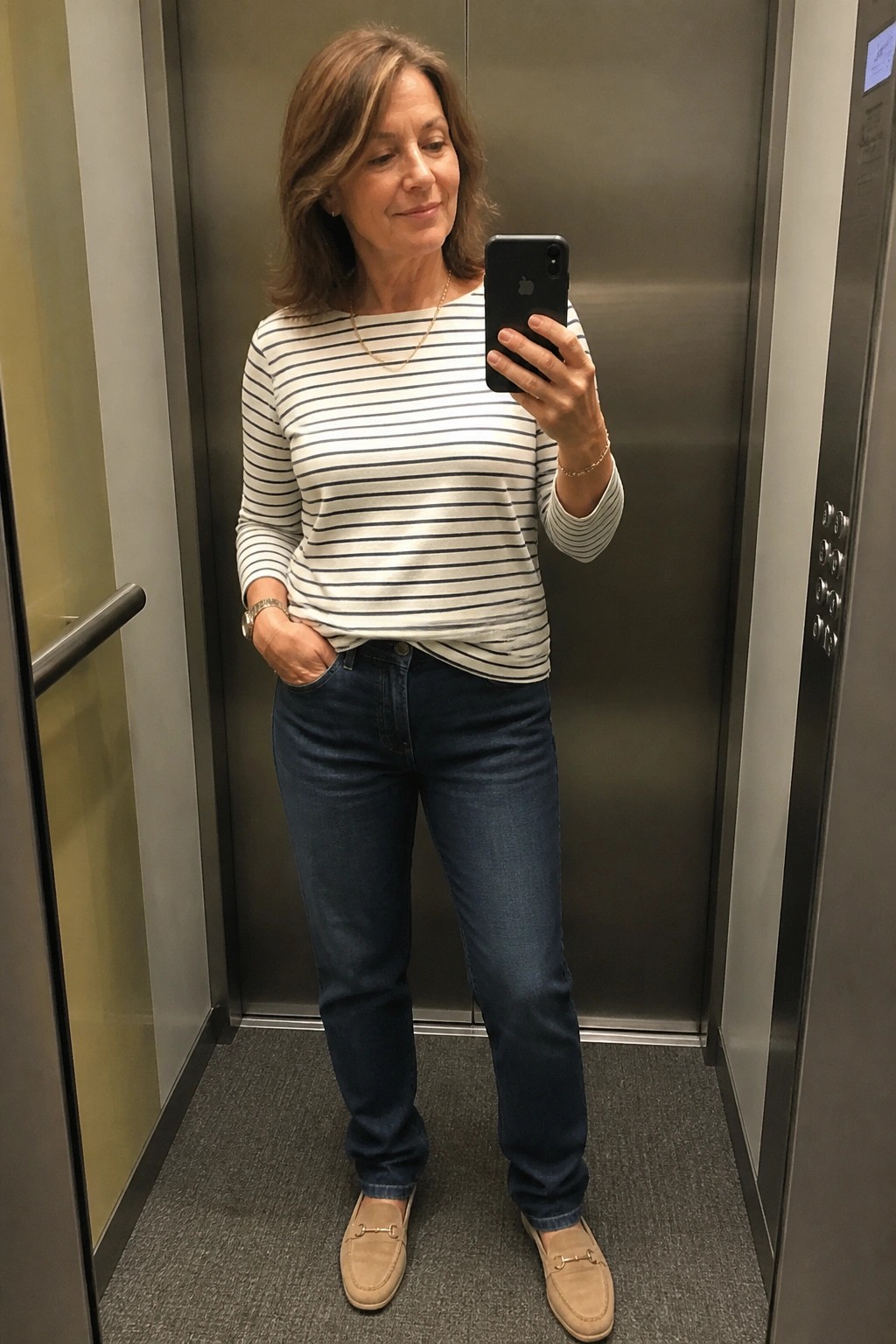 Woman in striped shirt and jeans taking selfie in elevator