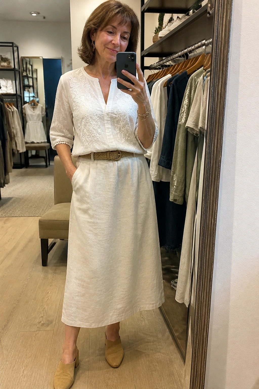 Woman in white embroidered blouse and skirt taking mirror selfie in boutique