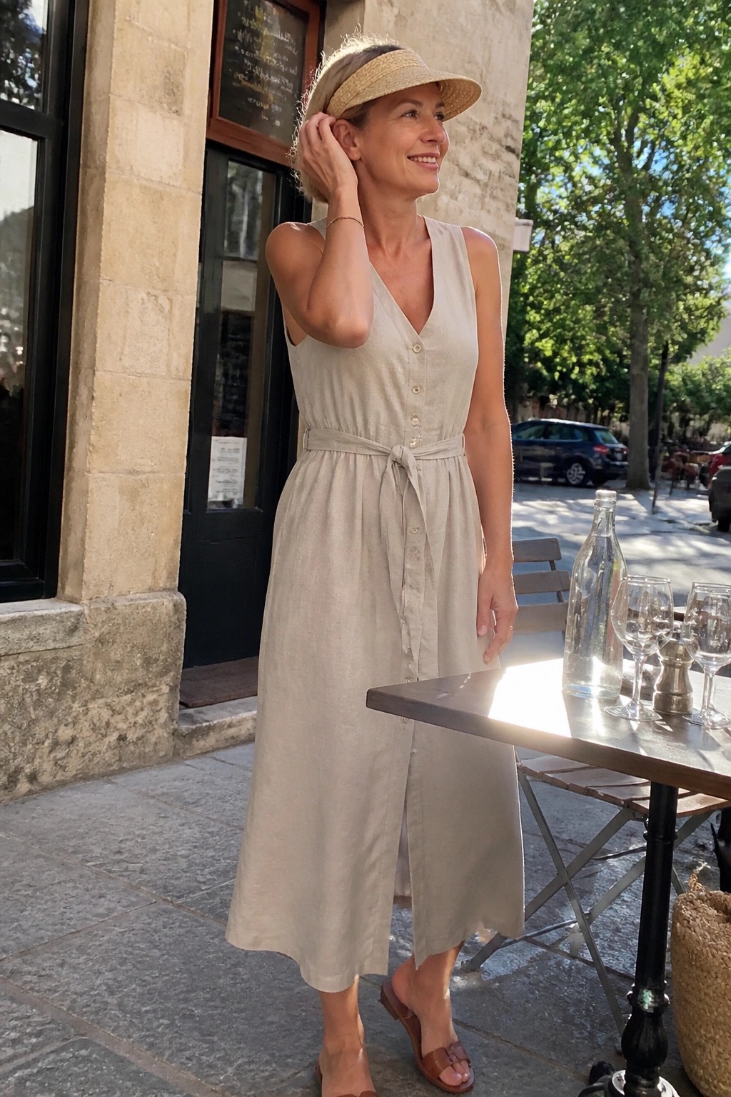 Woman in beige linen dress and straw visor at outdoor cafe table