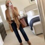 Silver-haired woman in cream turtleneck, camel cardigan, and jeans holding phone and bag
