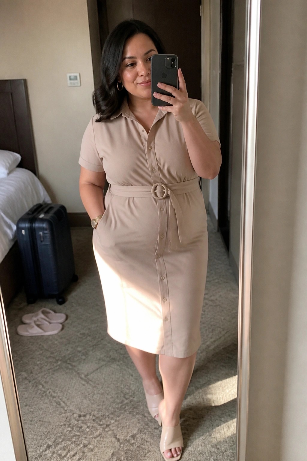Woman wearing a beige belted midi shirt dress with short sleeves and button front paired with nude open toe heels in a hotel room mirror selfie.