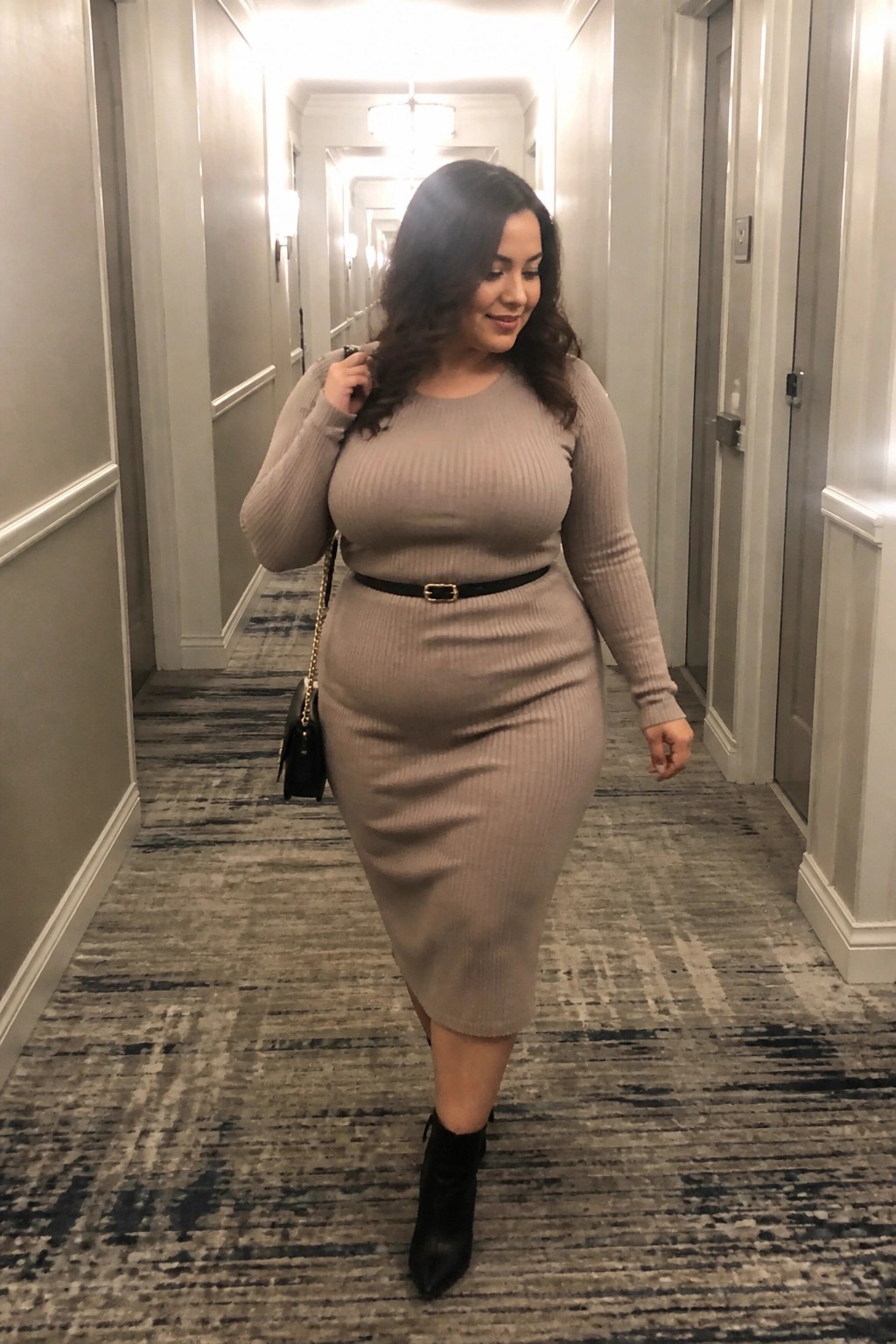 Woman in beige ribbed dress with black belt walking in hallway