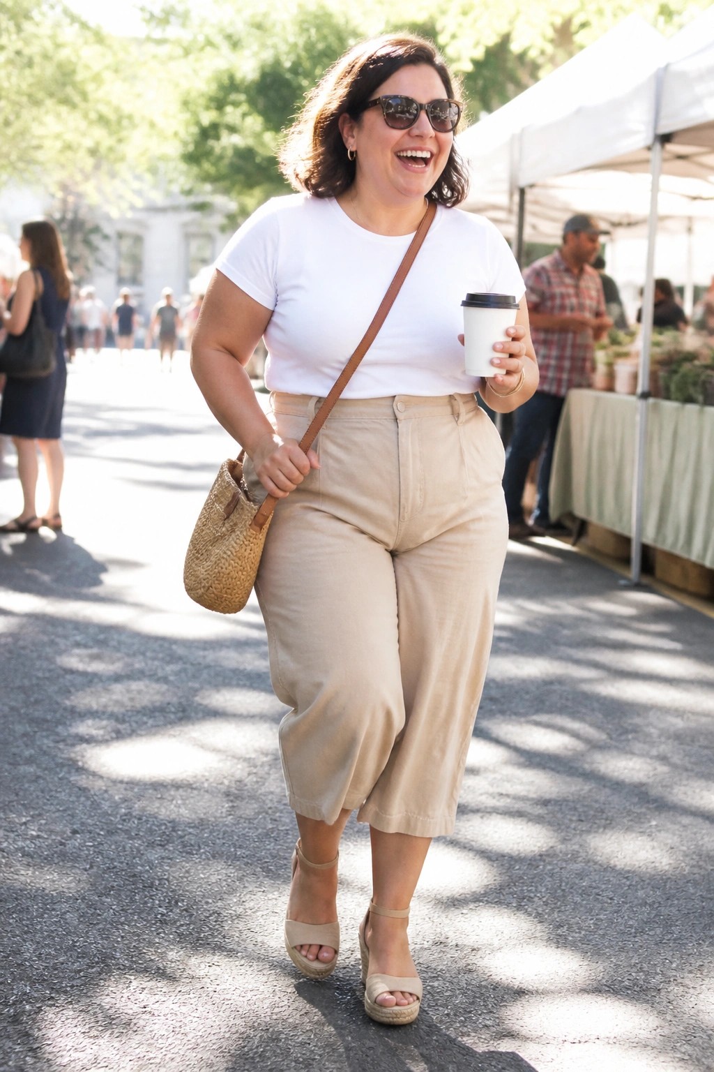 Plus size woman wearing a white tucked t-shirt with high waisted cropped khaki pants and beige wedge sandals carrying a straw crossbody bag.