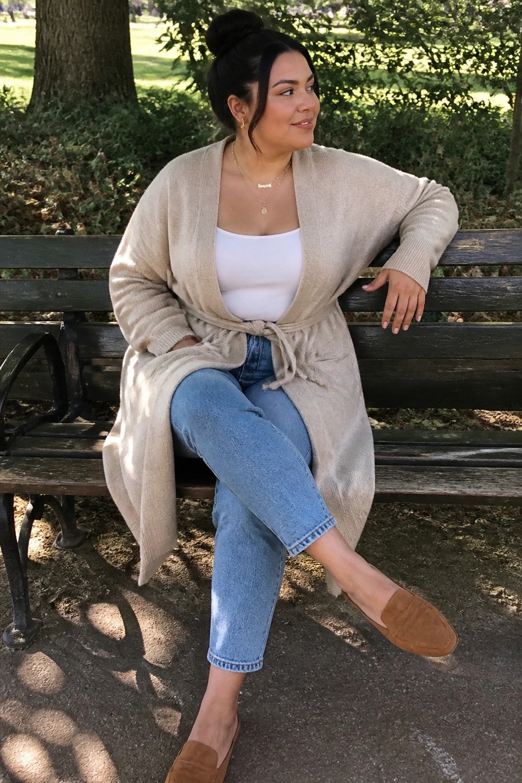 Woman in beige cardigan and blue jeans seated on park bench