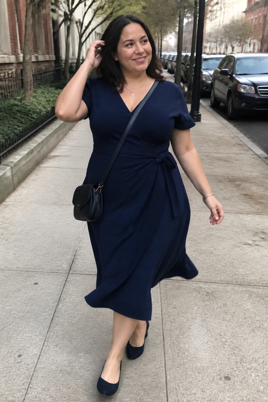 Woman in navy blue wrap dress with black bag on city sidewalk