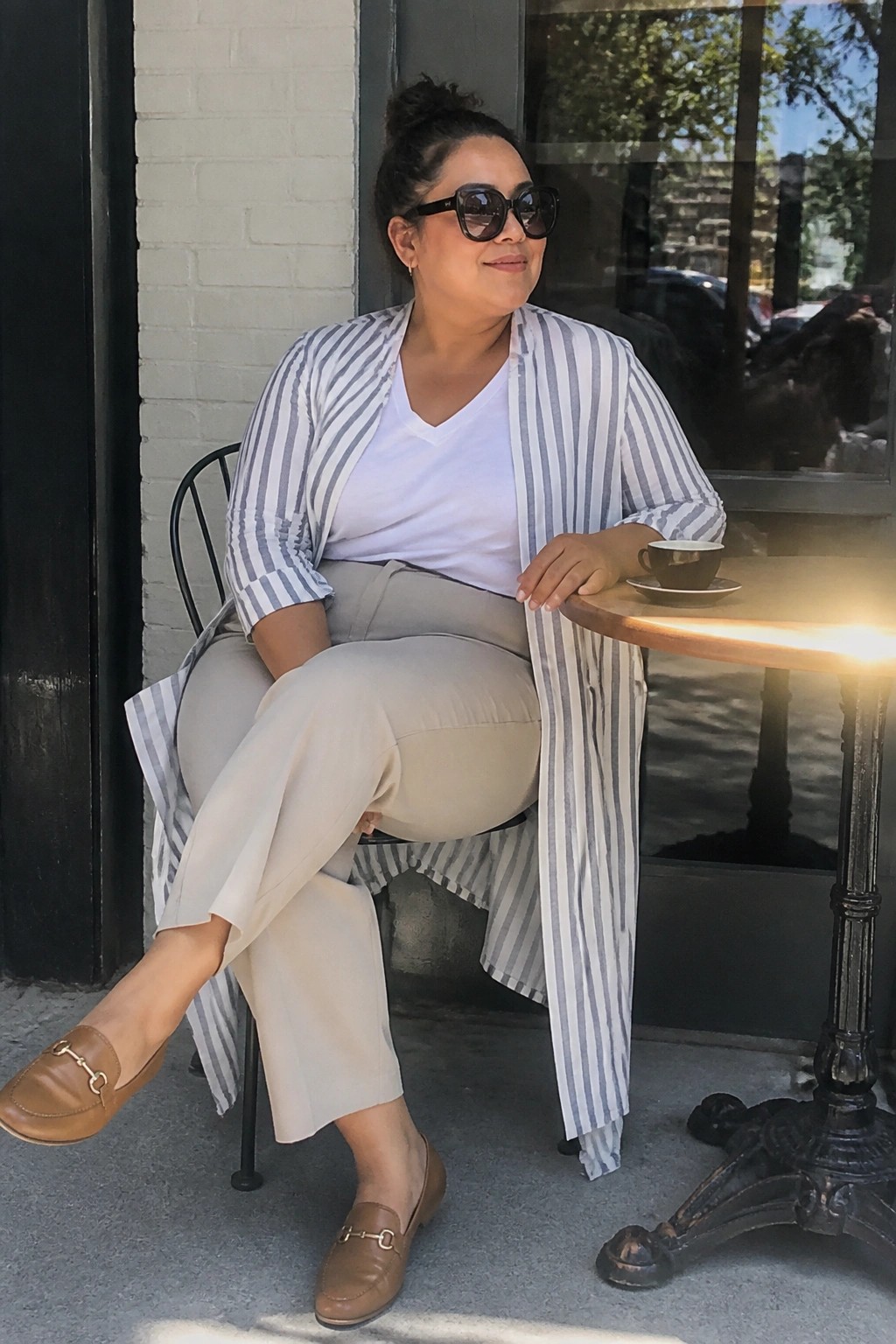Woman in striped cardigan and beige pants at outdoor cafe table with coffee