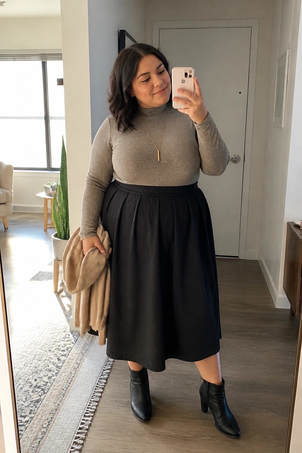Woman in gray turtleneck and black midi skirt taking mirror selfie with phone
