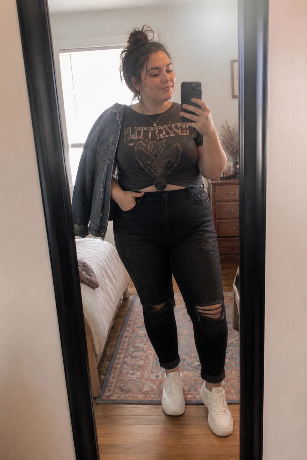 Woman in Led Zeppelin tee and ripped jeans taking bedroom mirror selfie
