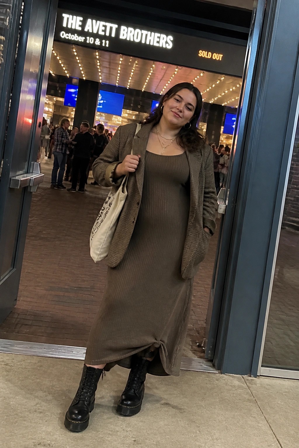 Woman in brown dress and plaid blazer at sold-out Avett Brothers venue entrance.