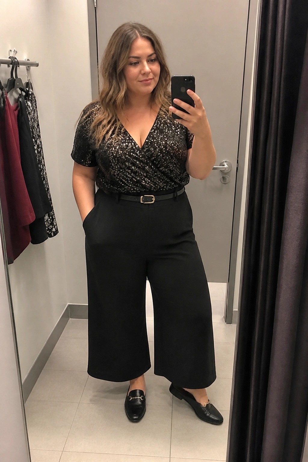 Woman taking mirror selfie in black sequined top and wide-leg pants.