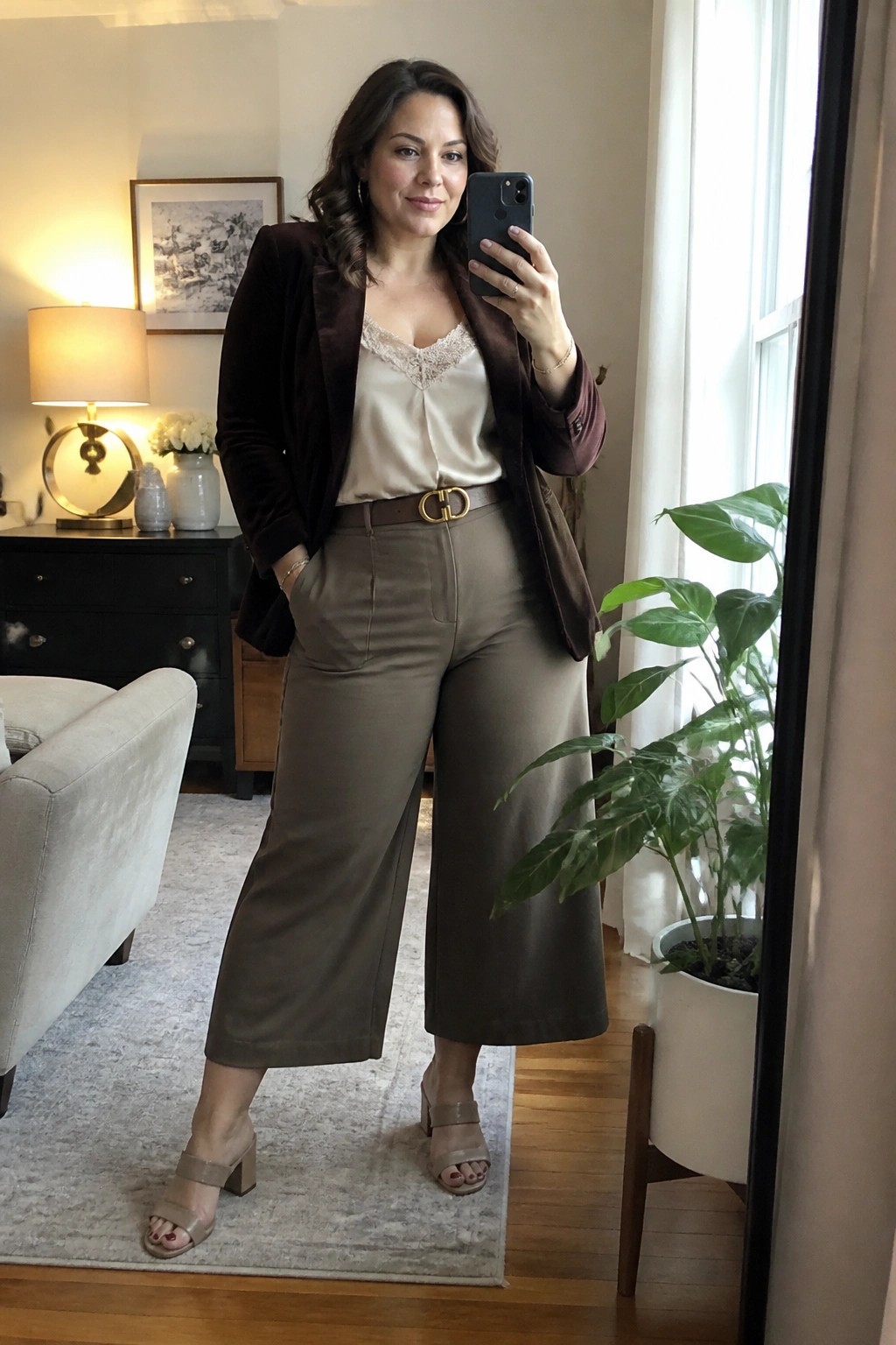 Woman in brown velvet blazer and wide-leg pants taking mirror selfie indoors