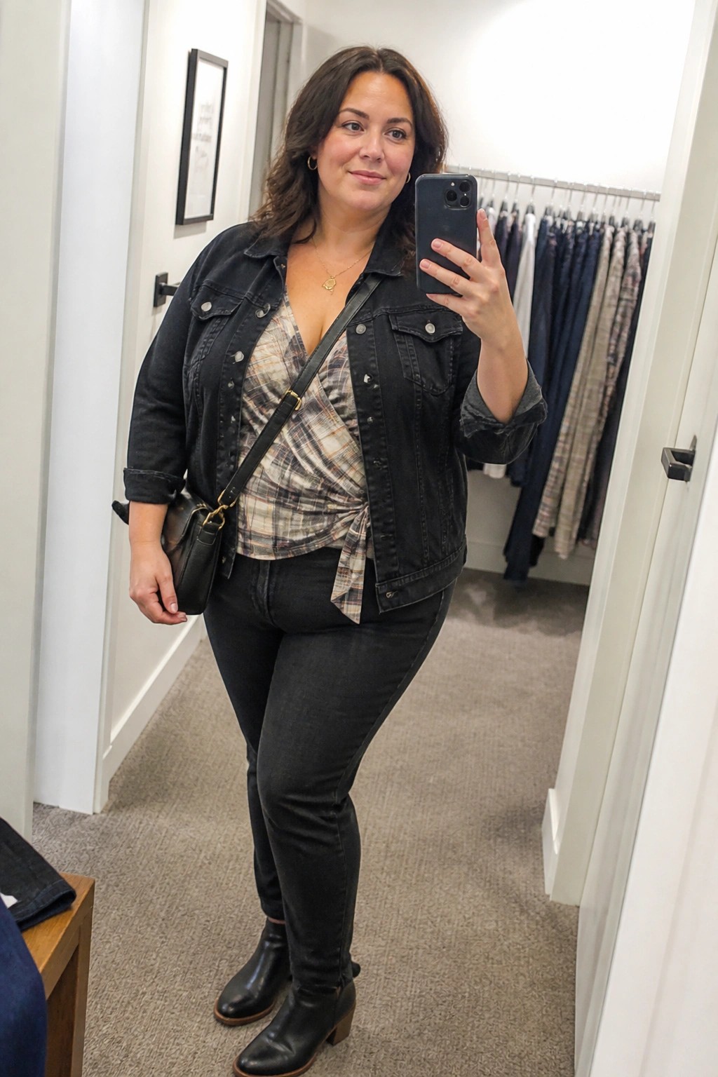 Woman in black denim jacket and plaid top taking mirror selfie in store