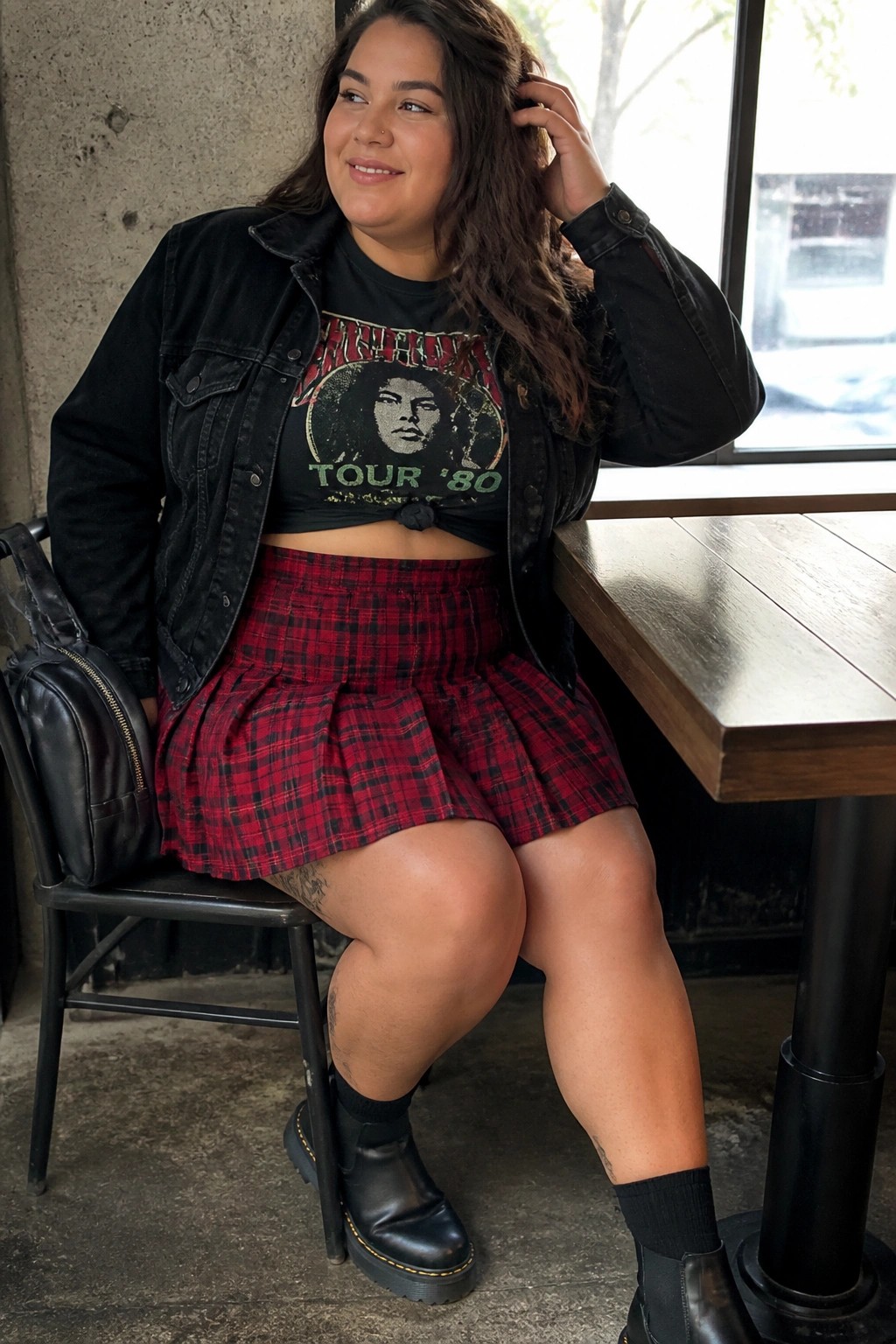 Woman in black jacket and red plaid skirt seated at wooden table indoors