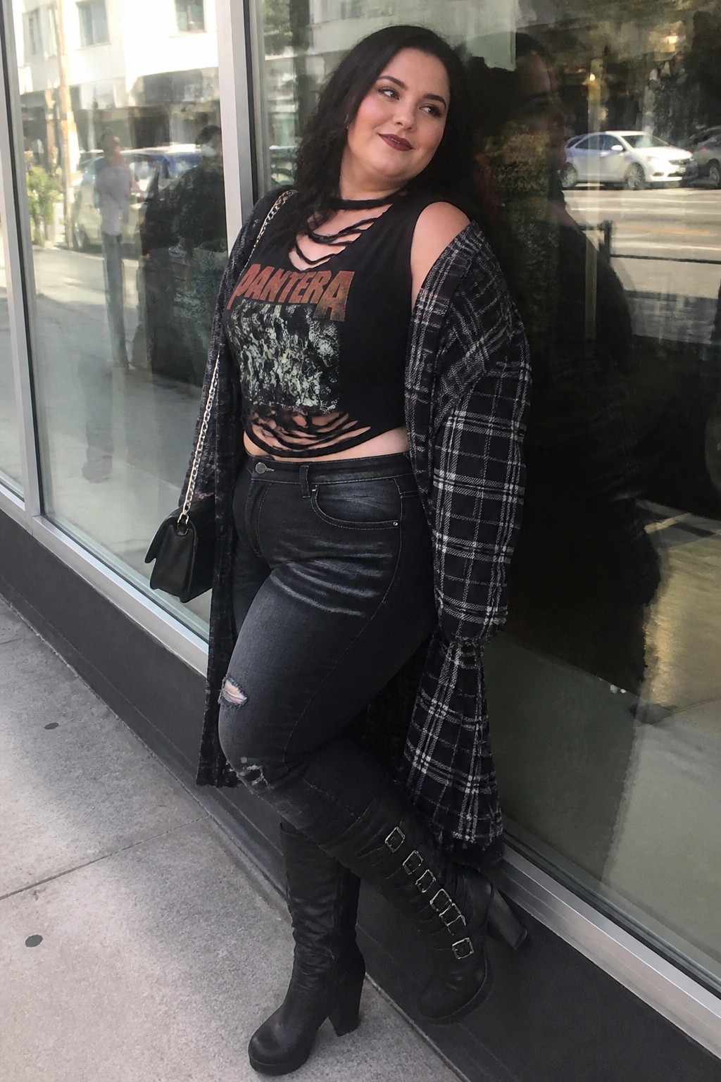 Woman in cutout Pantera crop top, plaid shirt, ripped jeans, and boots by window