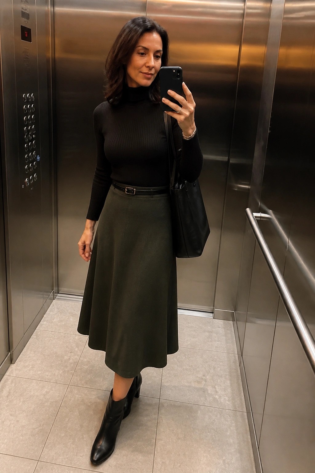 Woman in black turtleneck and green skirt taking selfie in elevator