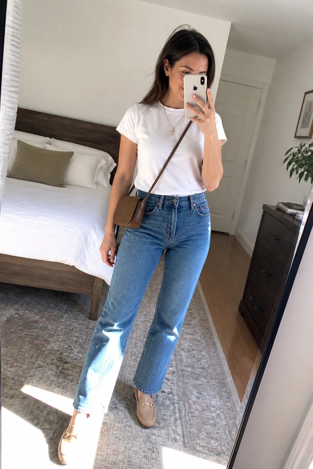 Woman in white t-shirt and blue jeans taking mirror selfie in bedroom