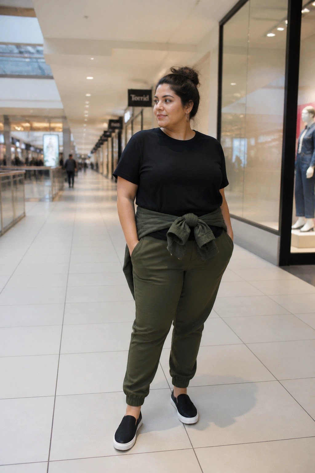 Plus-size woman in black tee and olive joggers with tied shirt in mall hallway