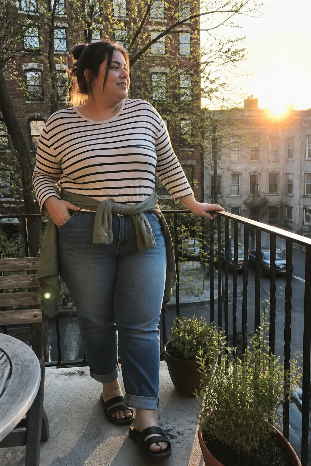 Woman in striped shirt and jeans on urban balcony at sunset with plants