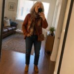 Woman in rust sweater and plaid scarf taking mirror selfie in hallway