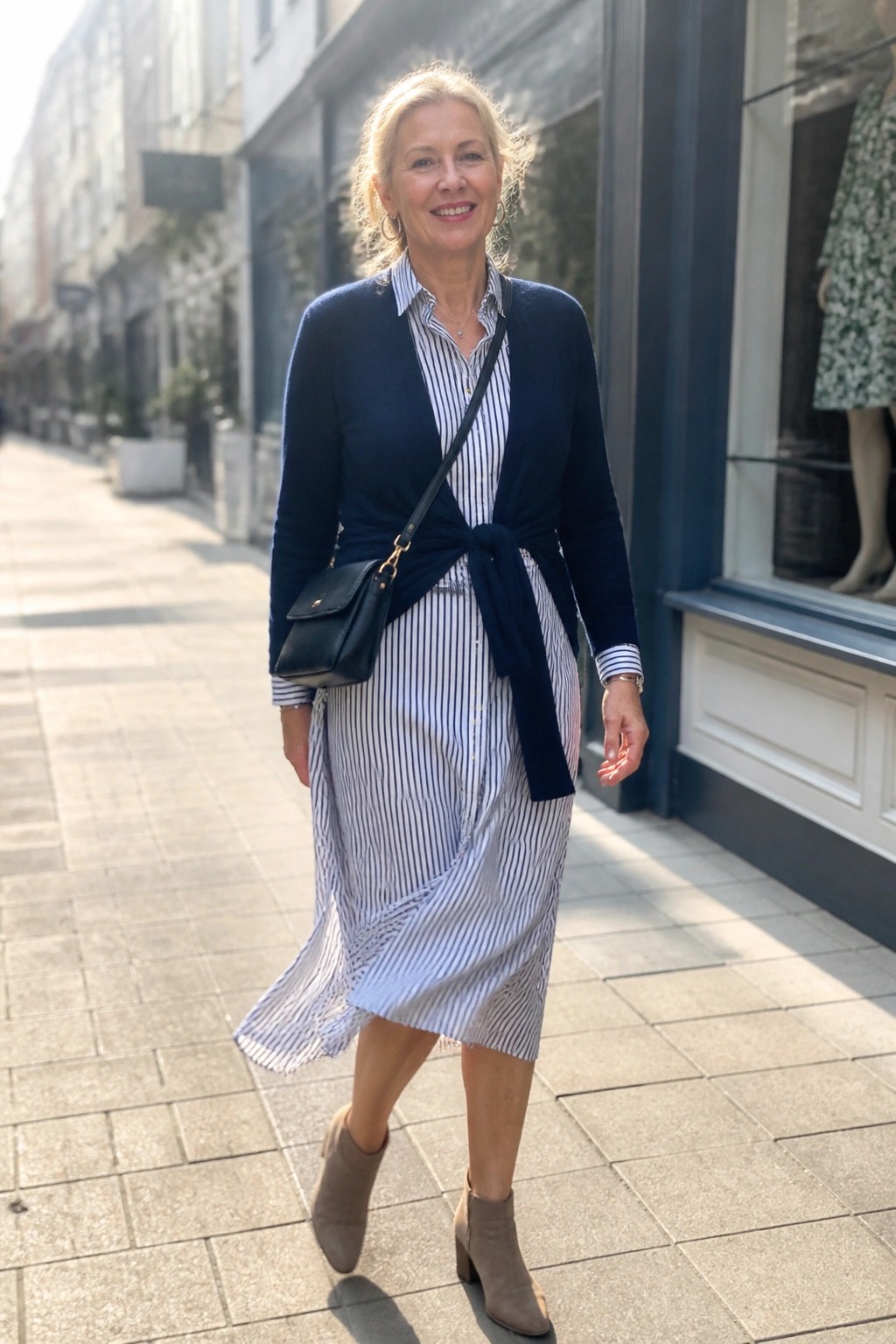 Blonde woman in striped shirt dress with navy tied cardigan on urban sidewalk