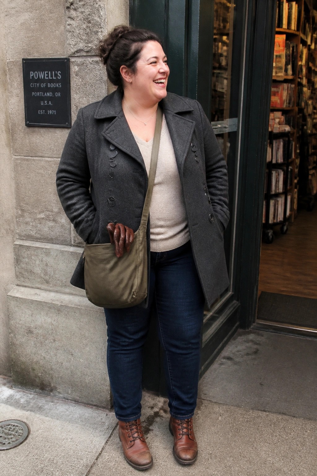 Smiling woman in gray coat with green bag outside Powell's City of Books.