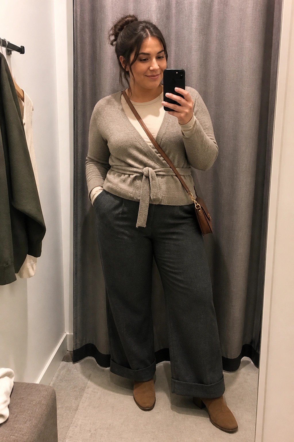 Woman in gray wrap sweater and wide-leg pants taking mirror selfie in fitting room