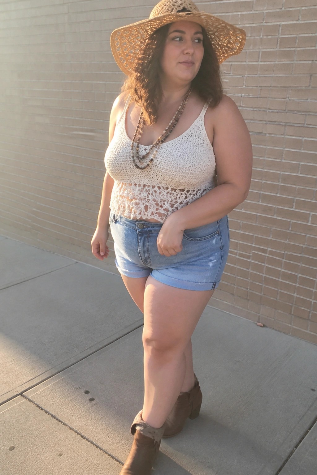 Curvy woman in white crochet crop top, denim shorts, boots and straw hat