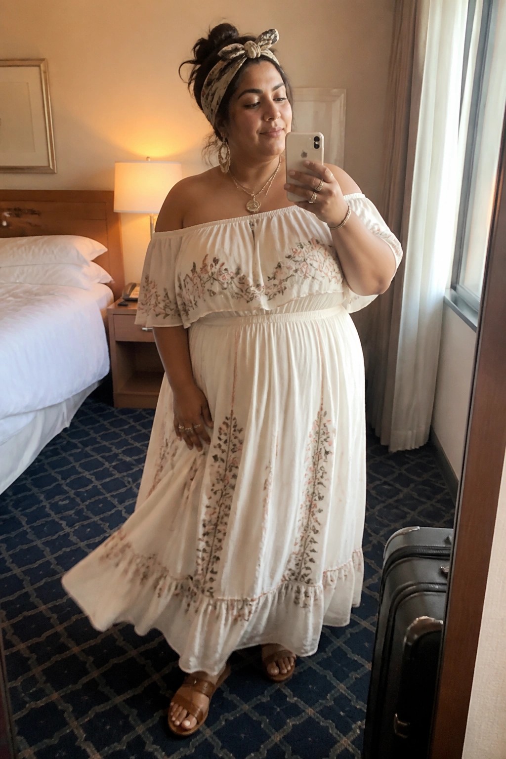 Woman in white off-shoulder floral maxi dress taking mirror selfie in hotel room