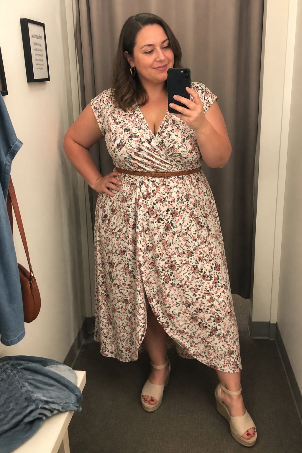 Woman in floral wrap dress taking mirror selfie in fitting room