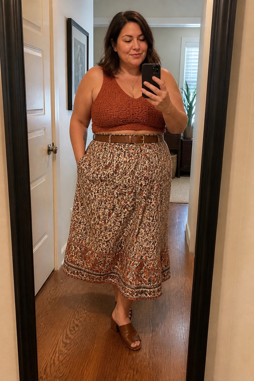 Woman in rust crochet crop top and floral skirt taking mirror selfie with phone