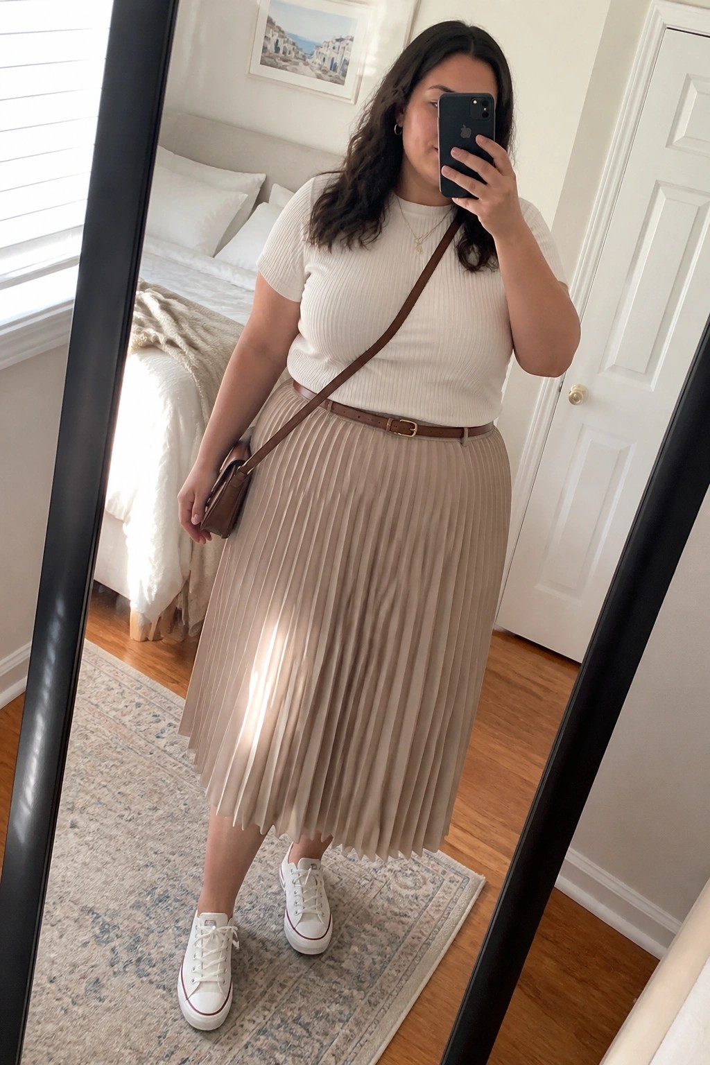 Woman taking mirror selfie in white top, beige pleated skirt, and sneakers