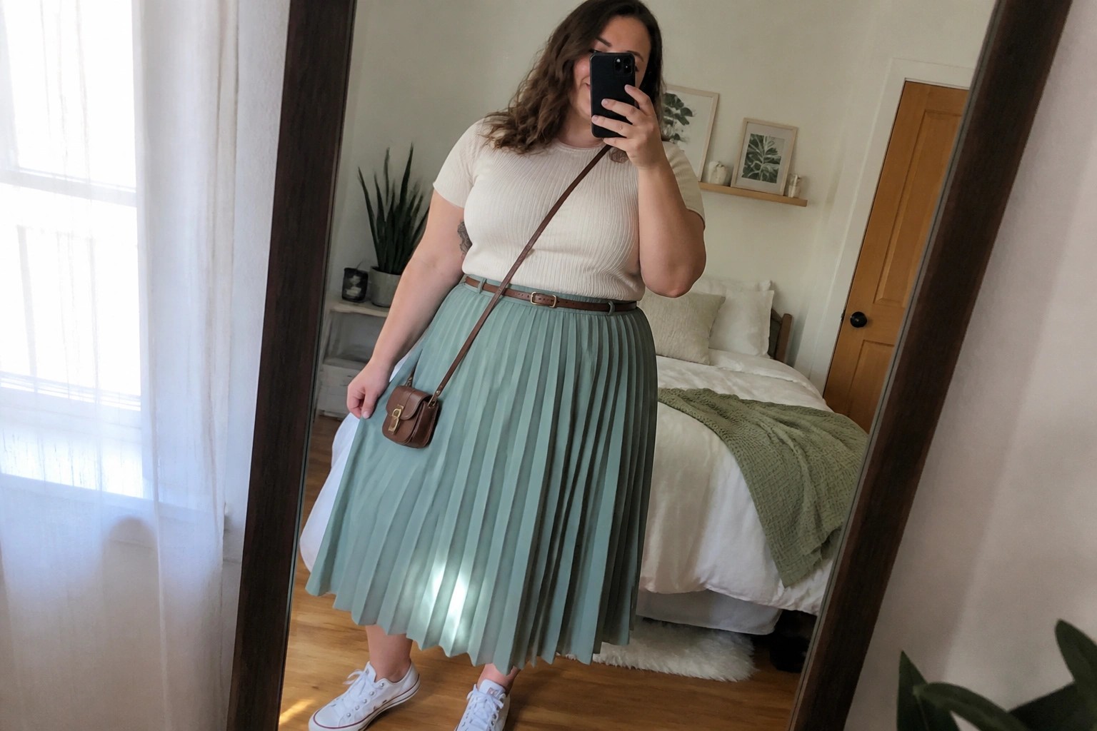 Woman taking mirror selfie in white top, beige pleated skirt, and sneakers